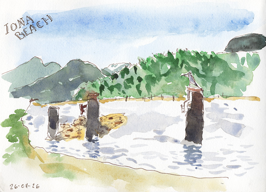 Ink and watercolor landscape sketch labeled “Iona Beach,” showing water, several dark wooden posts, a tree-lined shore, and mountains in the distance. A Great Blue Heron is on a wooden pile.